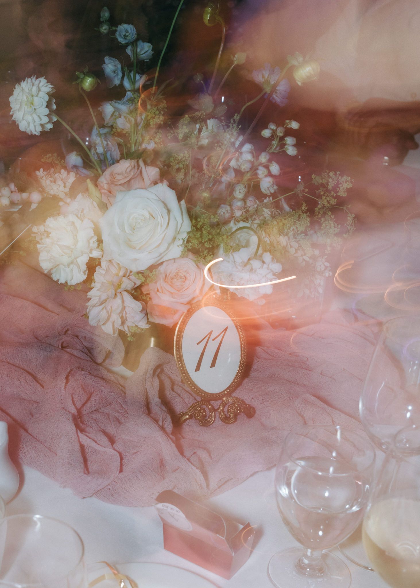 Elegant table setting with wine glasses and floral decorations in soft pink lighting.