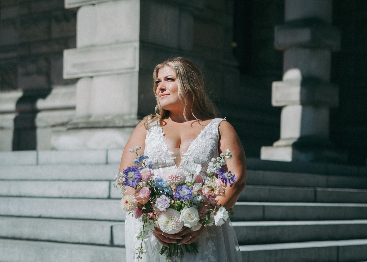 Wedding bouquet with purple and white flowers against stone architecture.