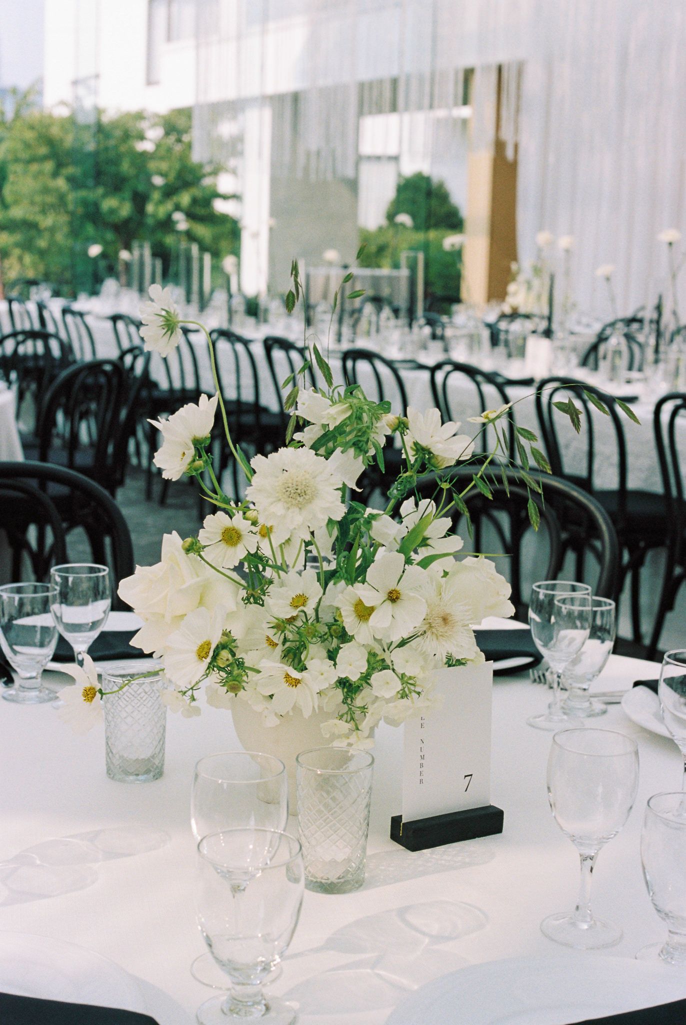 Elegant wedding reception tables with white floral centerpieces and black chairs.
