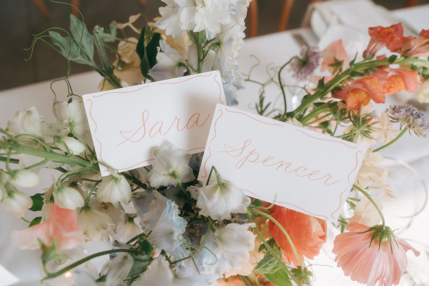 Elegant wedding place cards nestled among delicate floral arrangements with coral and white blooms and greenery.