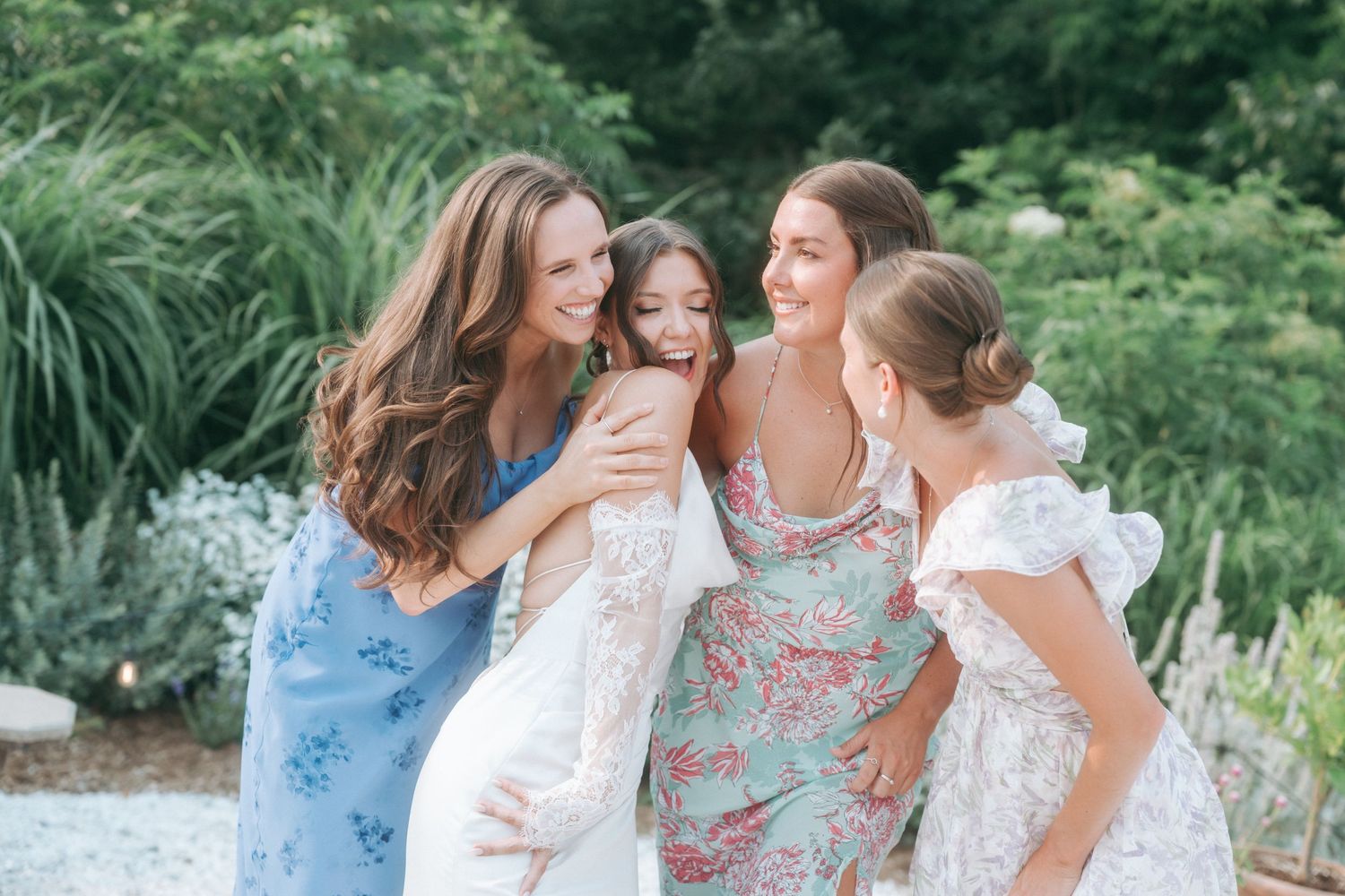 A group in coordinated white and floral outfits poses together in a lush garden setting during a summer photoshoot.