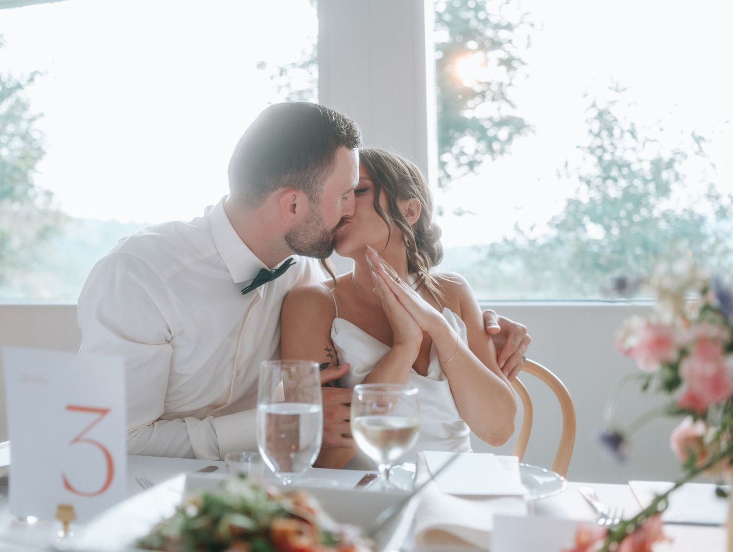 Romantic couple shares intimate moment during elegant wedding reception dinner at white-clothed table.