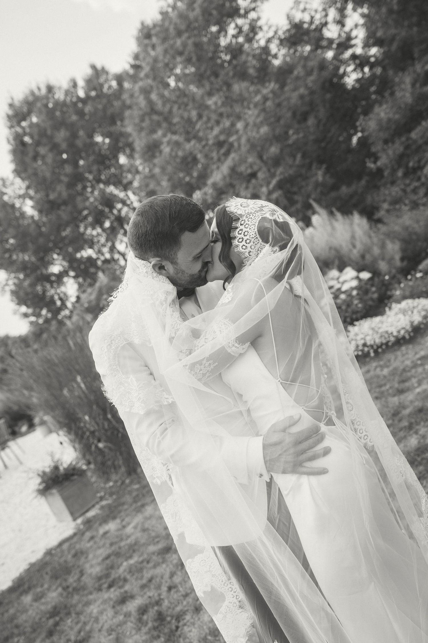 A romantic black and white wedding photo sequence showing a couple embracing under a flowing white veil in a garden setting.