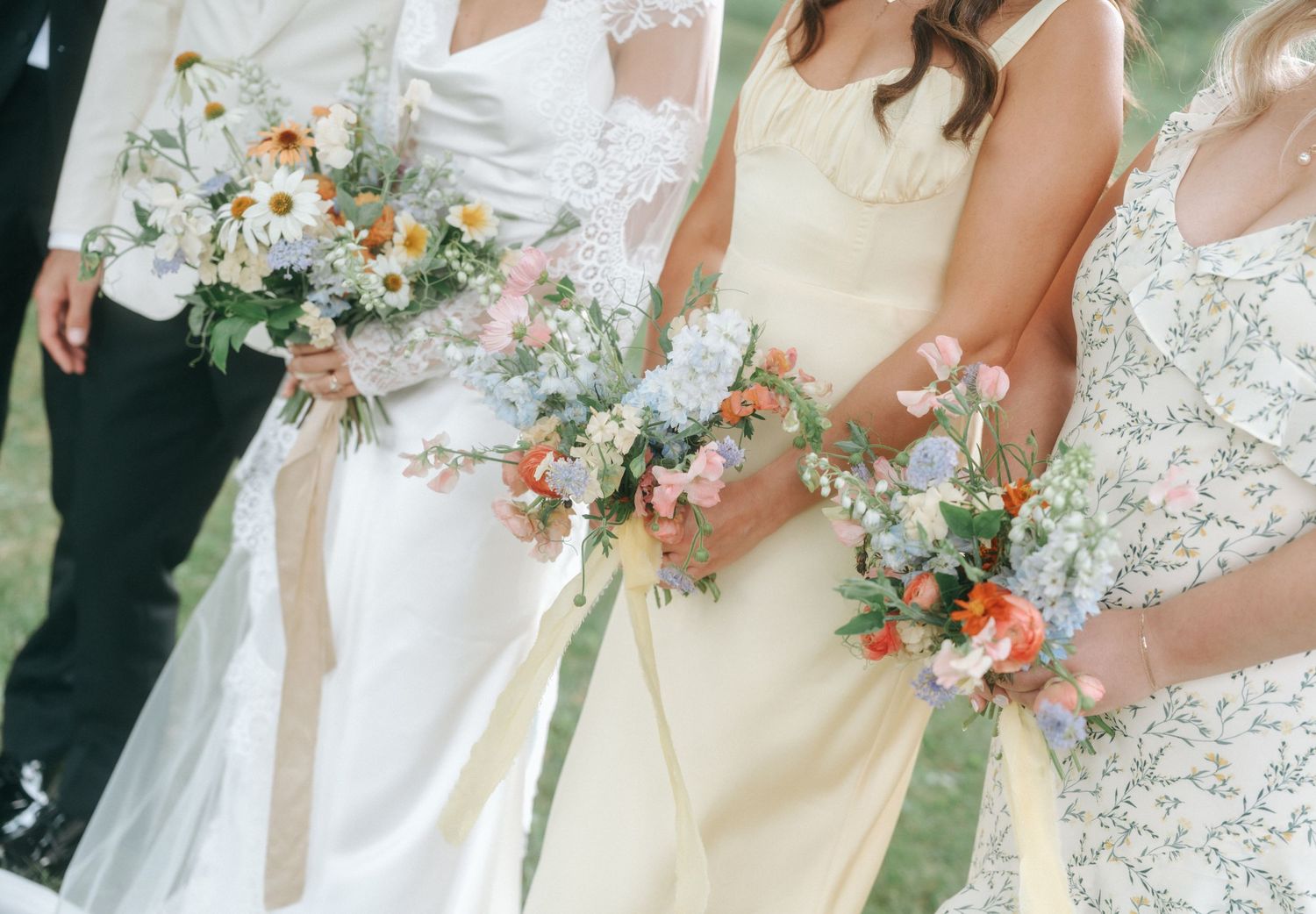 Wedding party stands in line outdoors holding colorful bouquets with pink and orange flowers against green background.