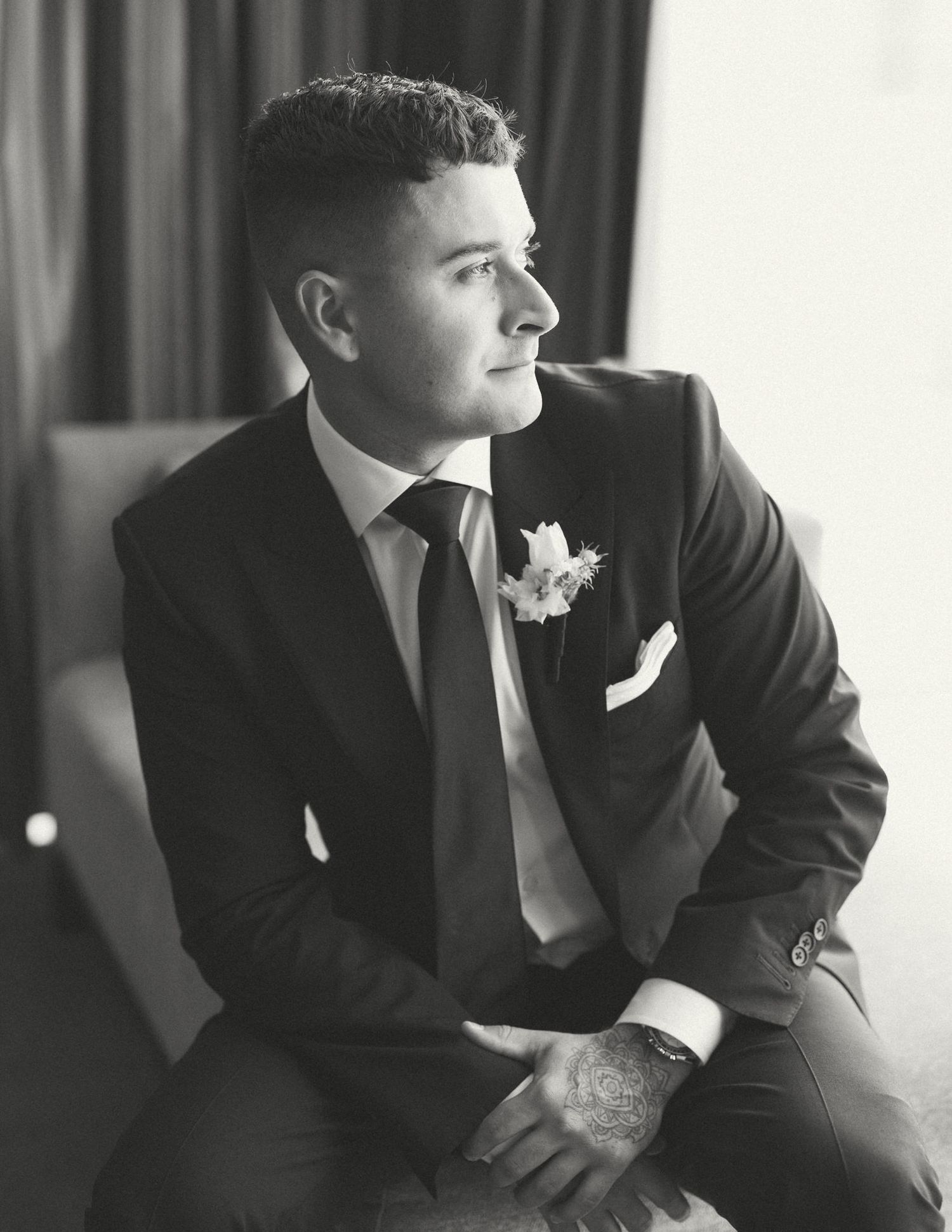 Black and white photo of groomsmen in suits sitting by a window.