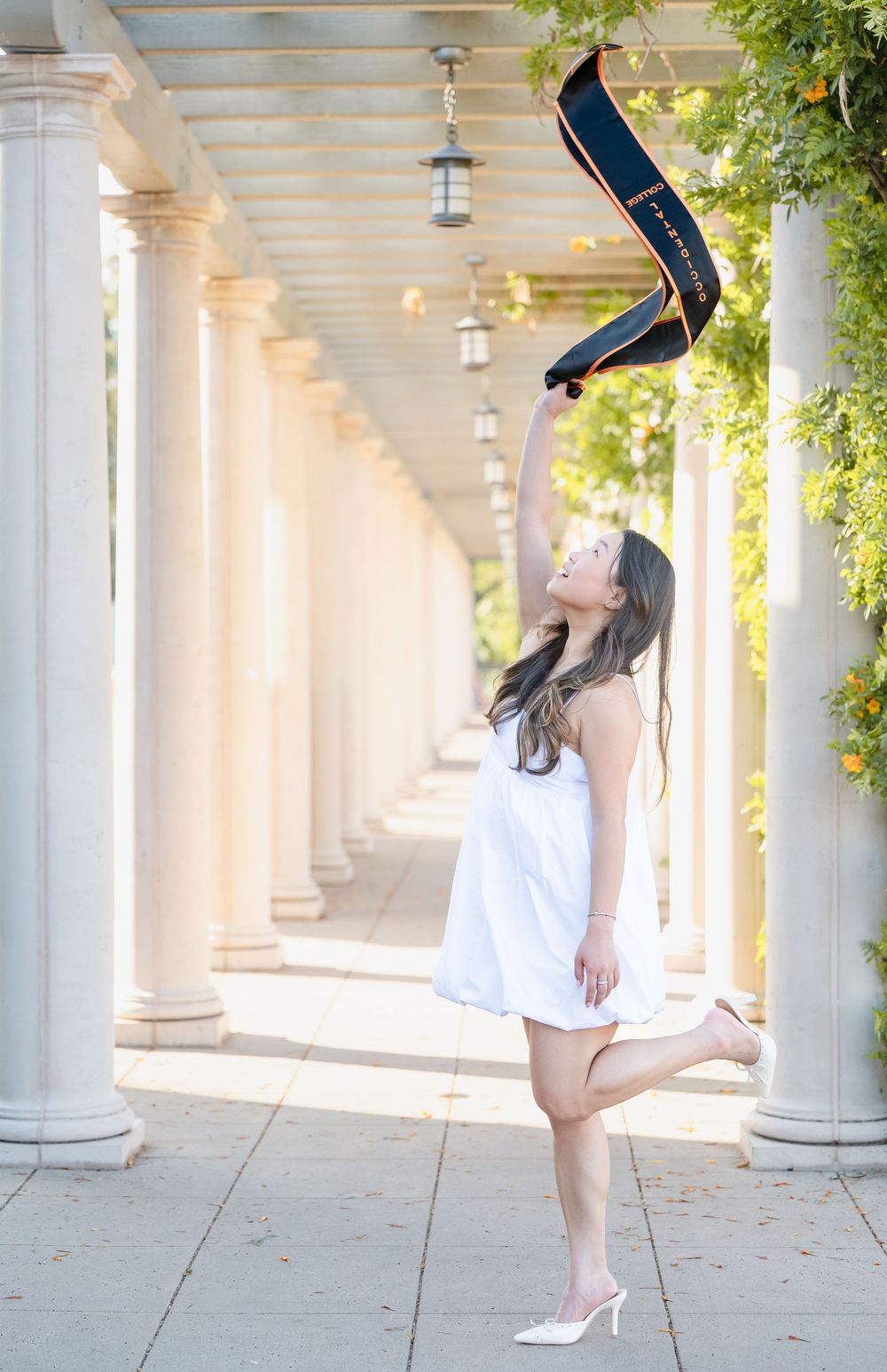 A person in a white dress performs a handstand against a backdrop of elegant columns and hanging greenery.