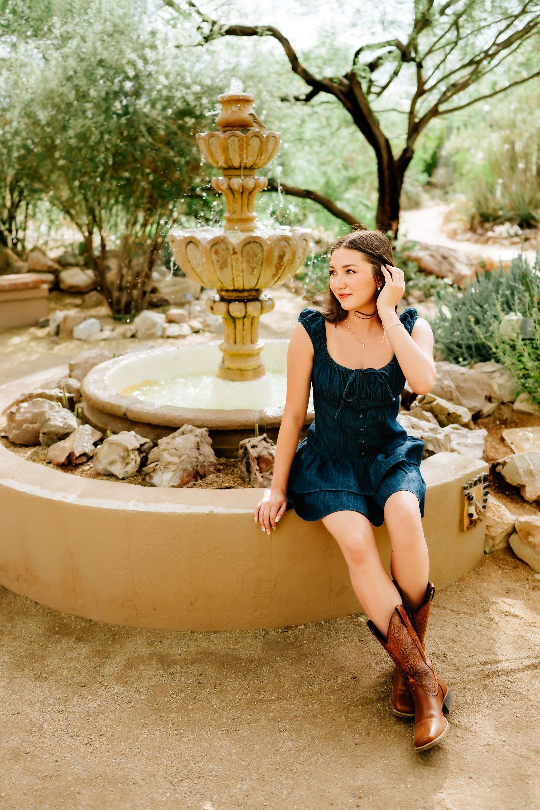 Tucson senior photographer capturing girl in navy dress by rustic fountain in desert garden