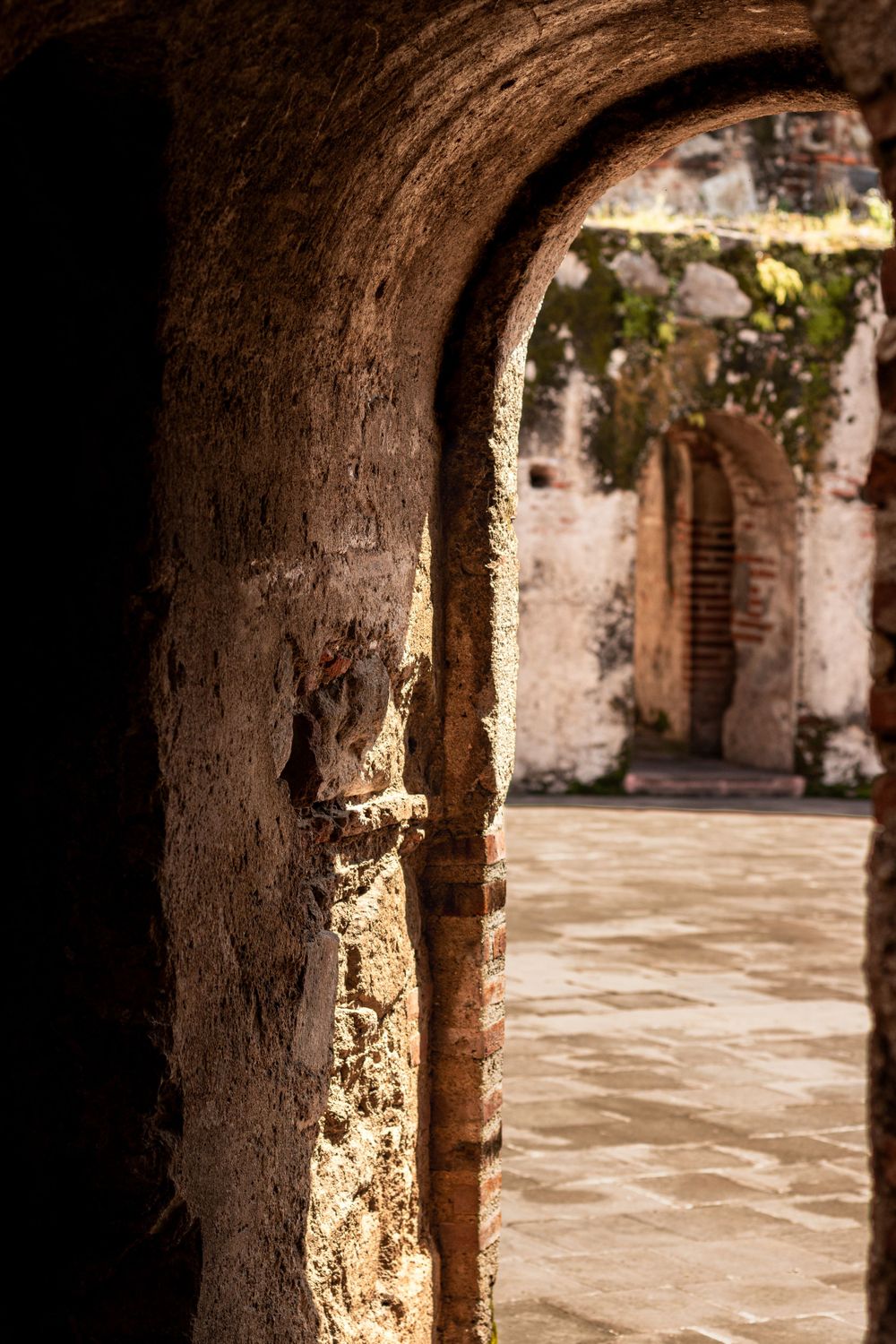 Stone archway corridor leading to a sunlit courtyard with rustic architectural details.