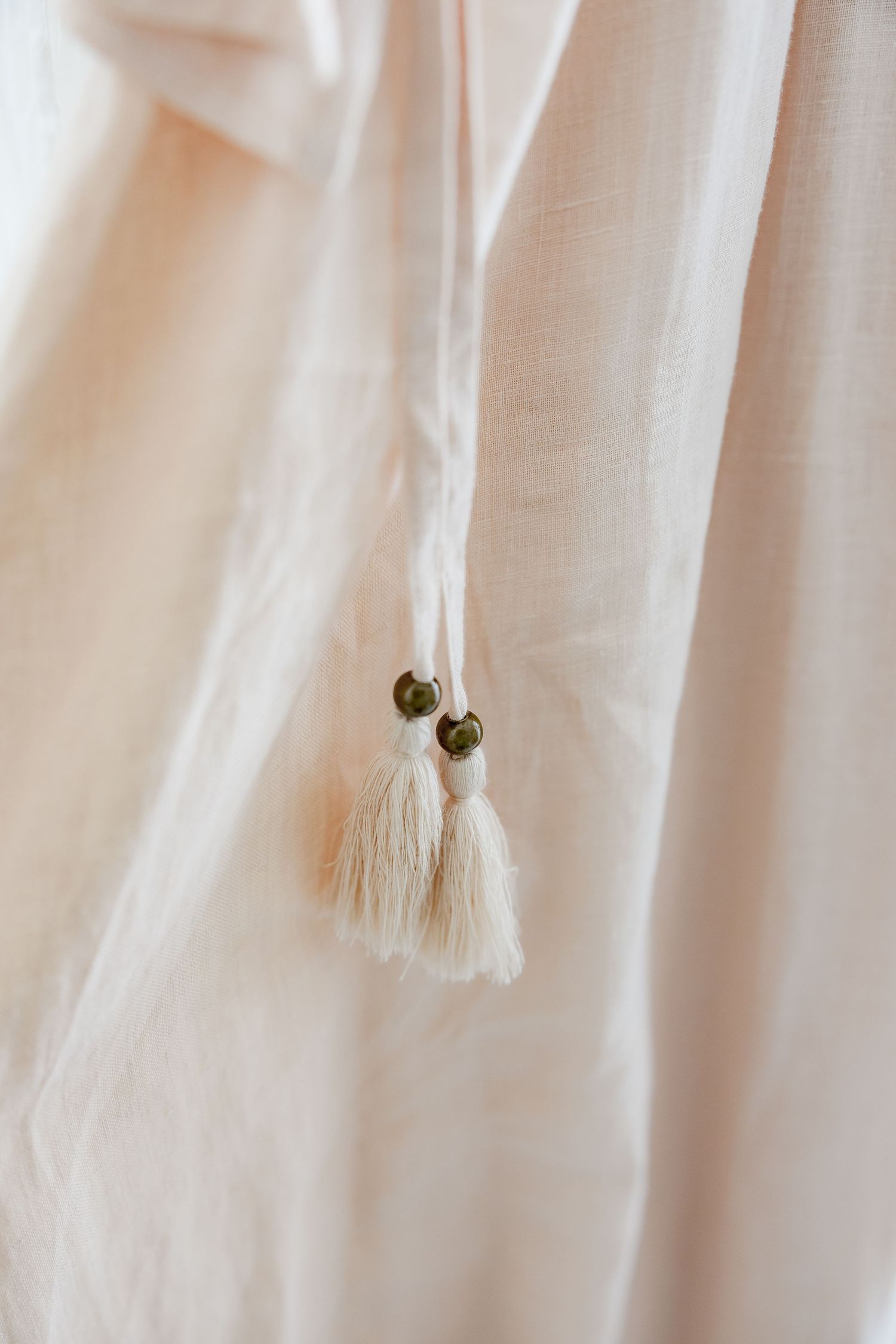 Small decorative tassels with beads hanging from white fabric.