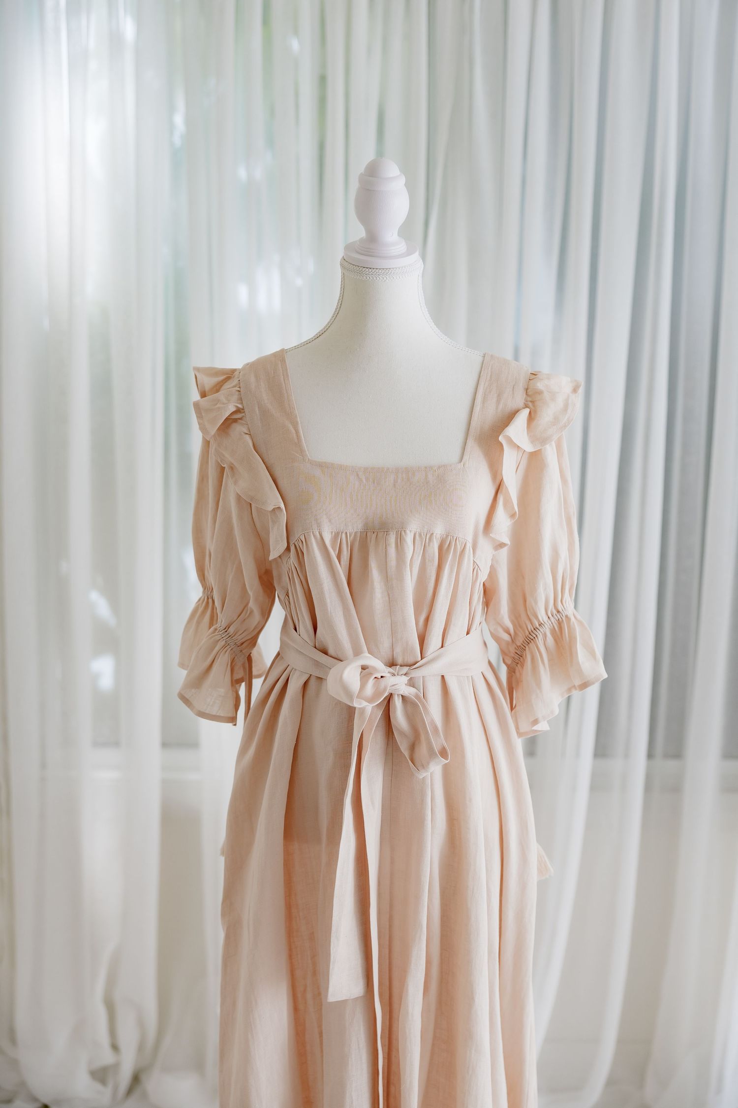 Vintage-inspired blush dress with square neckline and ruffle details displayed on dress form.