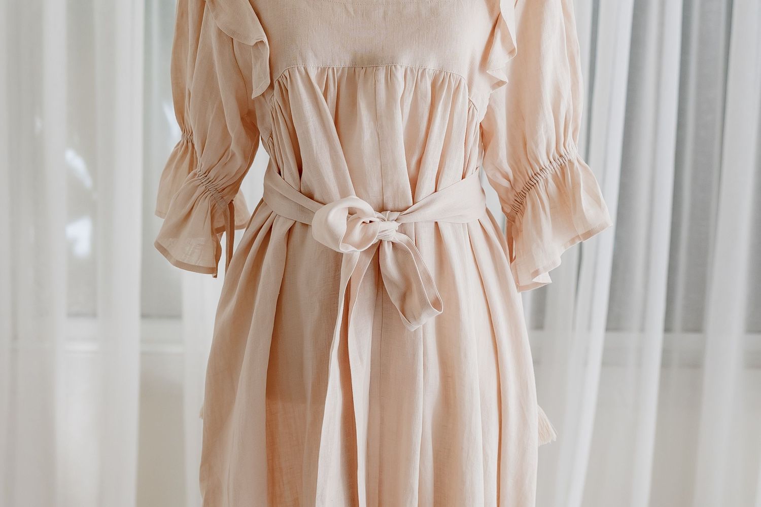 Close-up of pale pink dress showing ruffle sleeve and waist tie details.