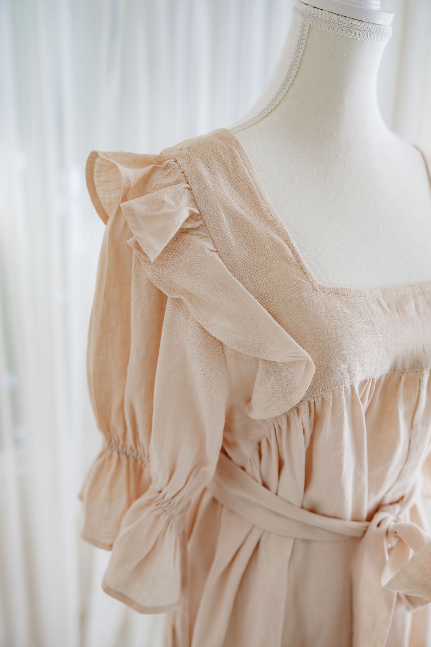 Close-up shot of blush dress neckline with delicate ruffle trim detailing.