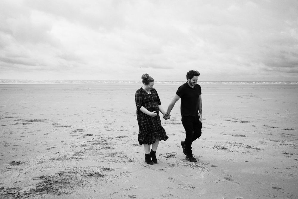Black and white photo of couple walking hand in hand on empty beach.