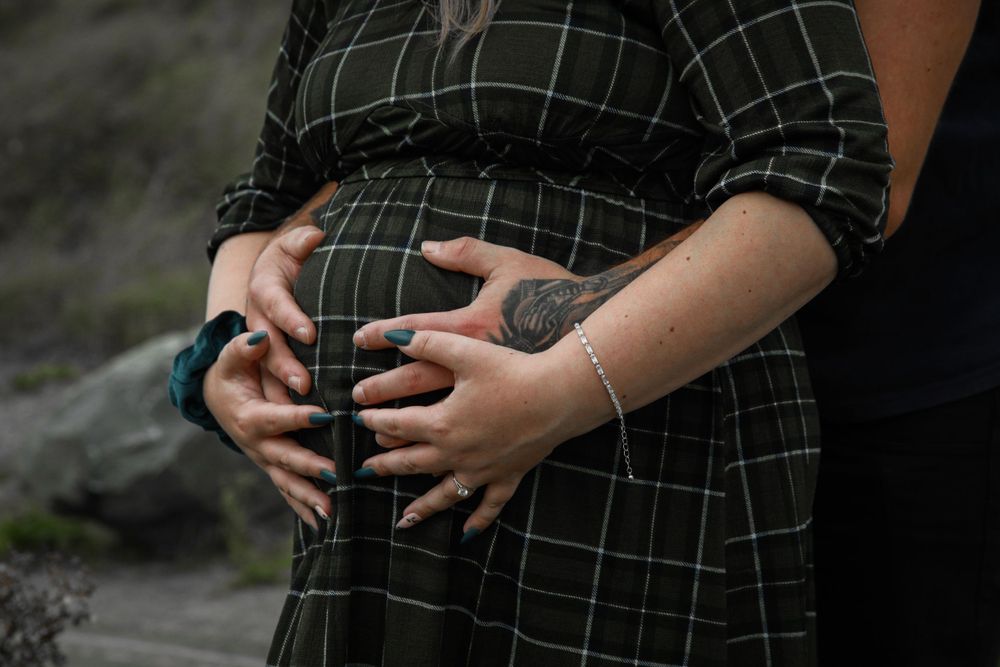 Close-up of hands tenderly cradling a pregnant belly in a plaid dress.