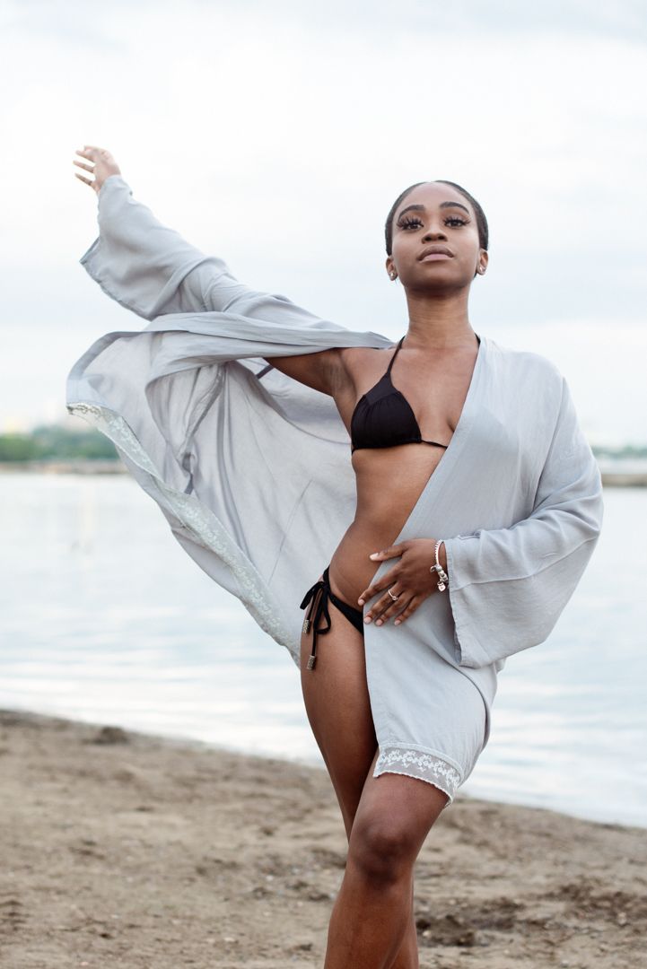 Figure in flowing white garment performs dynamic dance moves on beach.