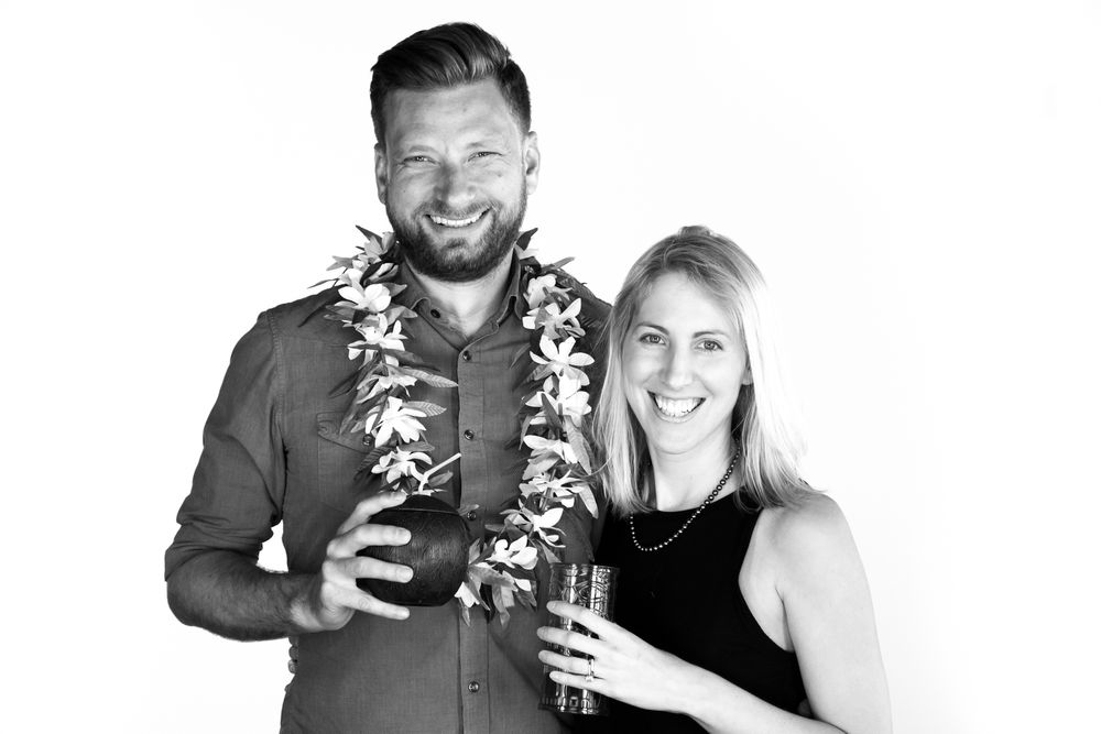 A black and white photo of a couple wearing Hawaiian leis and holding drinks at a celebration.