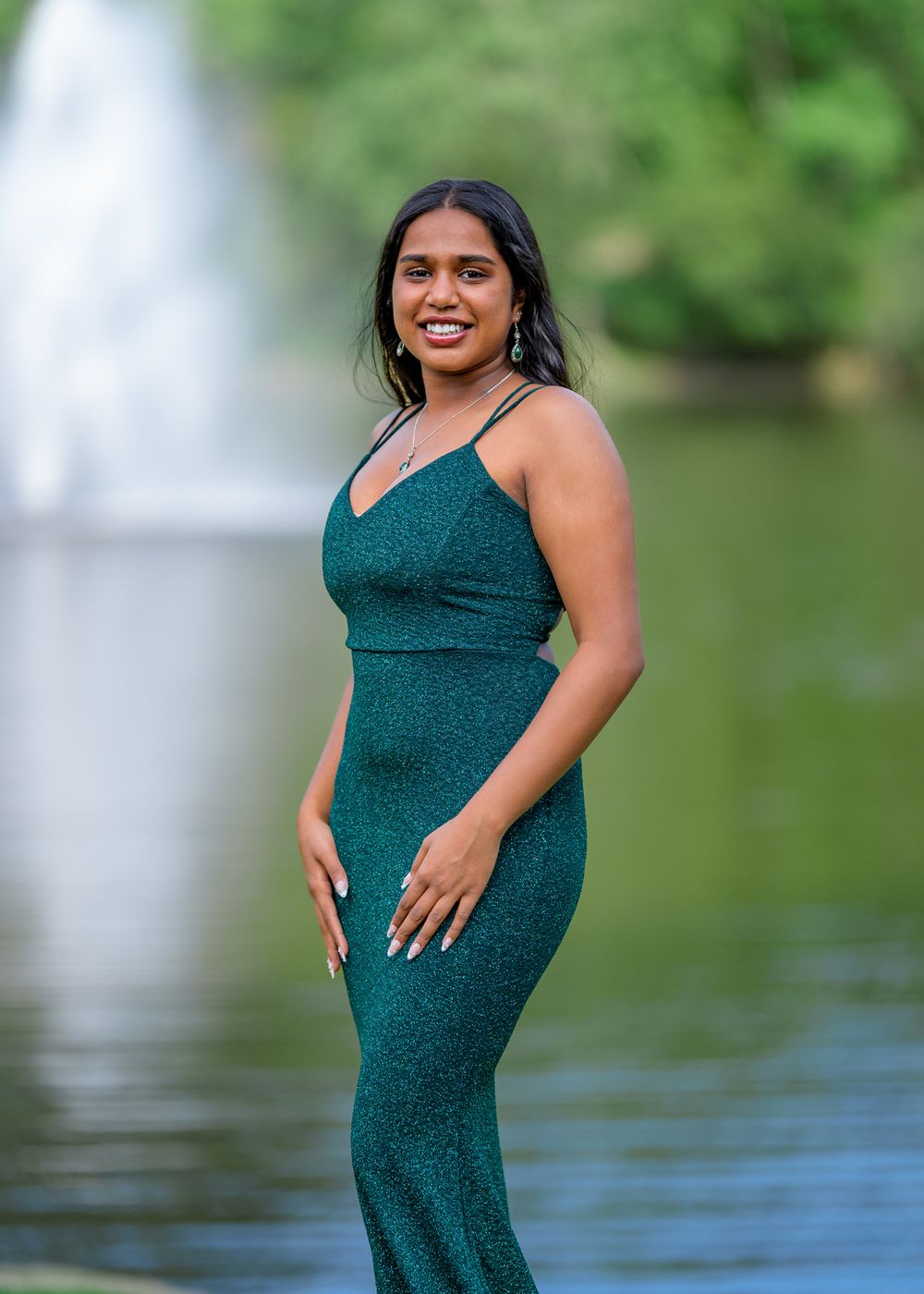 Elegant pose in fitted teal sparkle dress by waterfront setting.