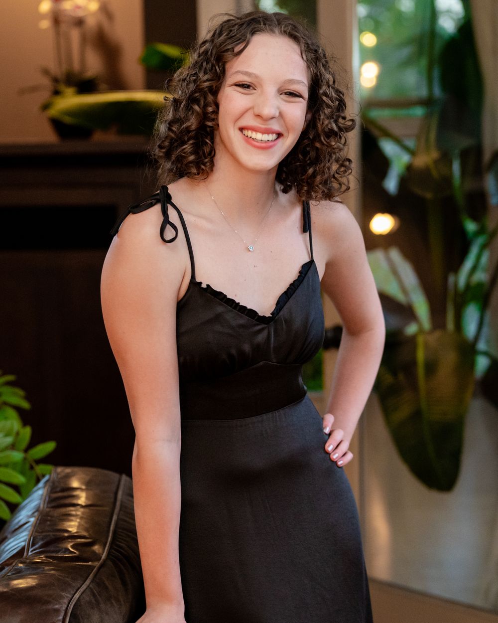 Portrait of person in black formal dress with curly hair against indoor background.