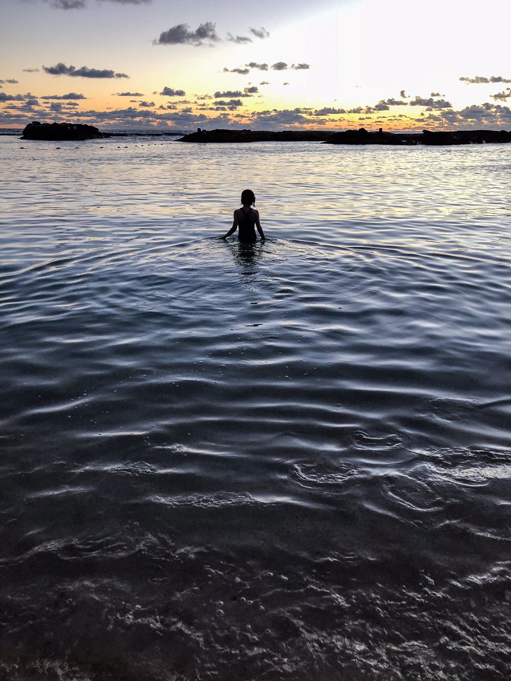 Silhouette of a person in water during sunset with dramatic cloudy sky.