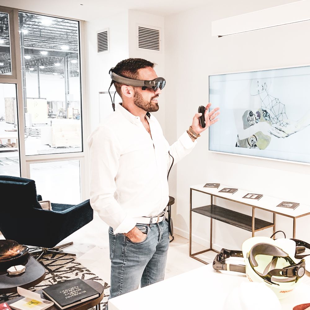 Person wearing VR headset while presenting content on a screen in a bright office setting.