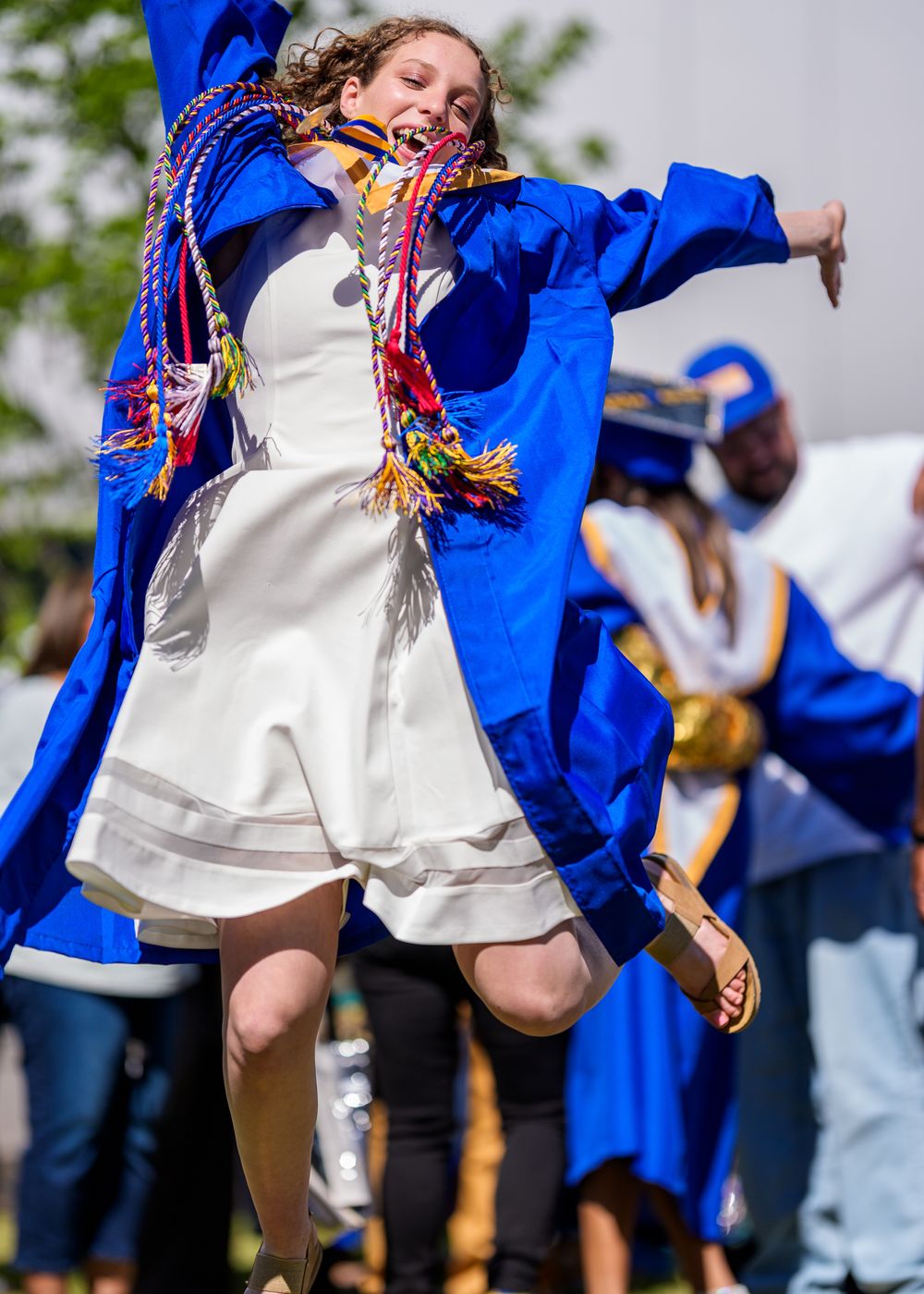 Dancer in blue robe and white outfit performs energetic traditional dance movement.