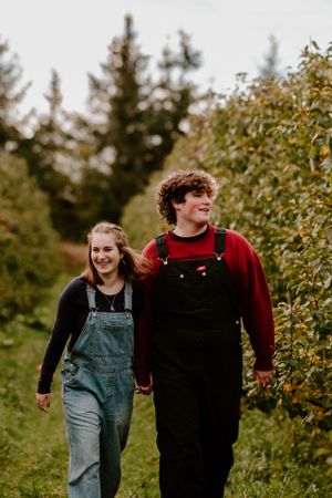 Two people walking and laughing together through an apple orchard on a sunny day.