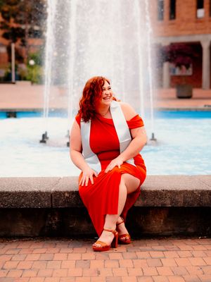 Fashion portrait session by a fountain featuring a bright red dress.