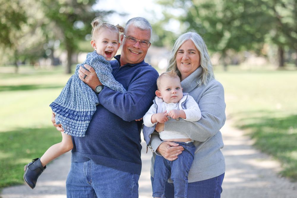 Family of four posing together on a sunny path surrounded by greenery.