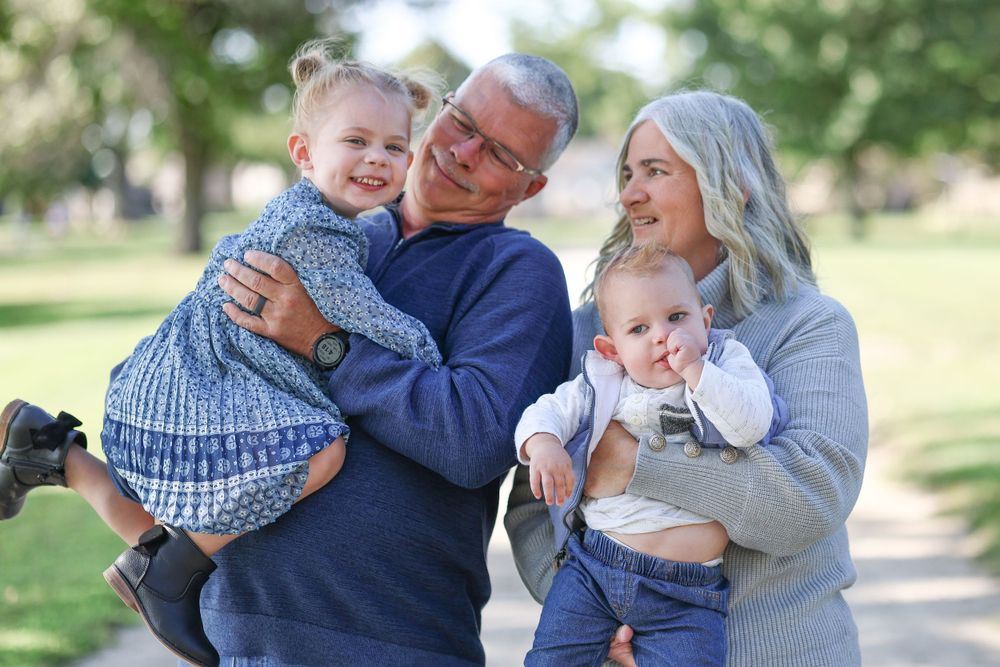 A loving family portrait outdoors featuring two young children with a couple in casual blue and gray clothing.