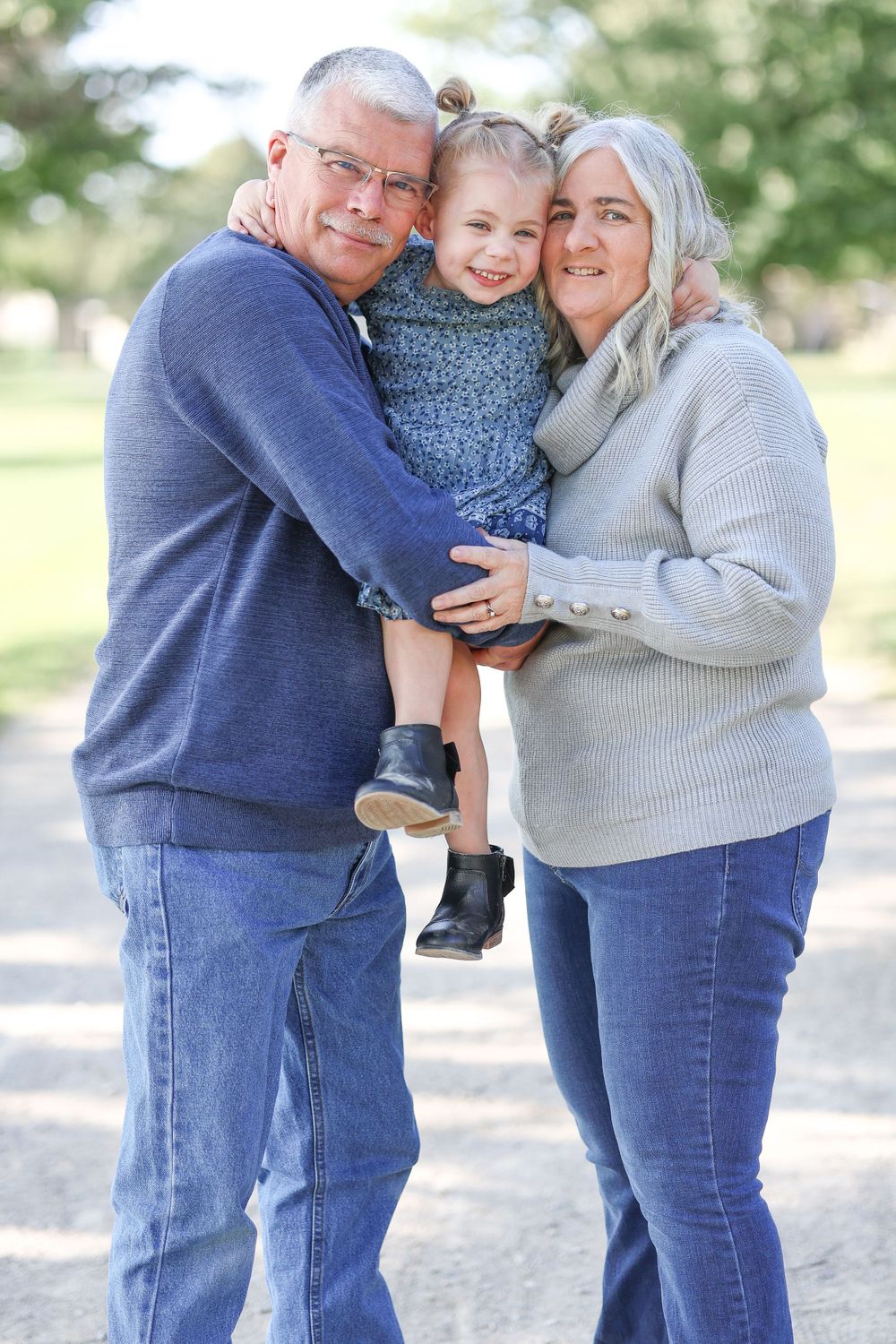 A couple in casual attire sharing a tender moment with a small child outdoors.