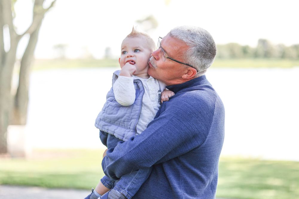 Adult in blue sweater holding and snuggling with baby in light blue outfit outdoors.