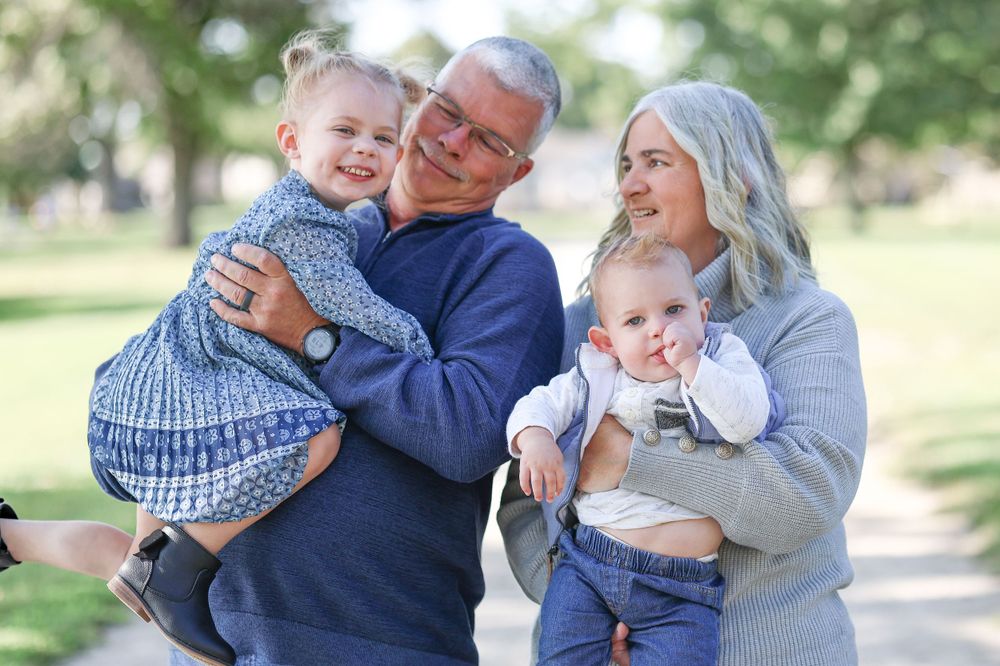 Family group hugging and smiling together on outdoor path in casual sweaters.