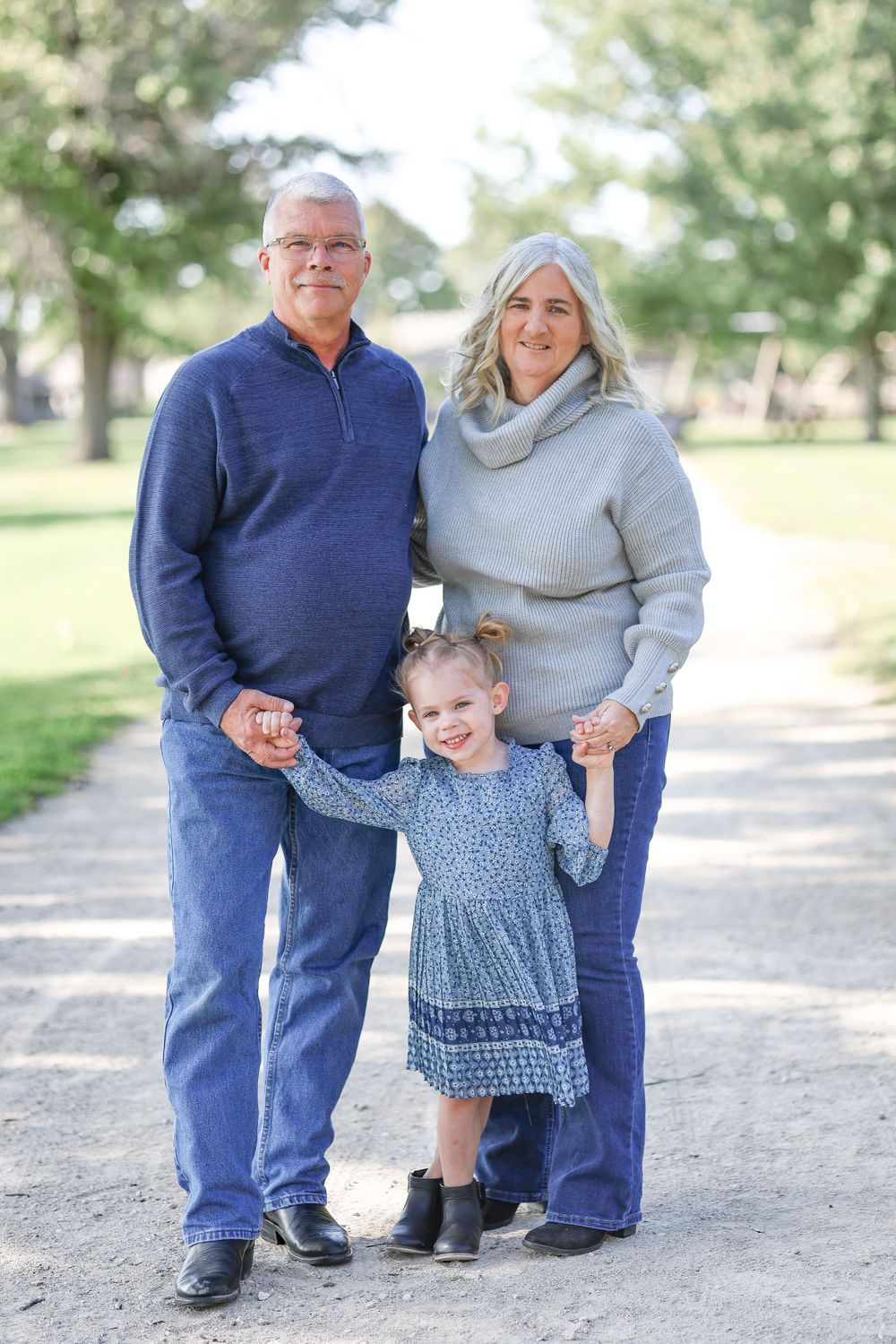 Three people holding hands while standing together on outdoor walking path.