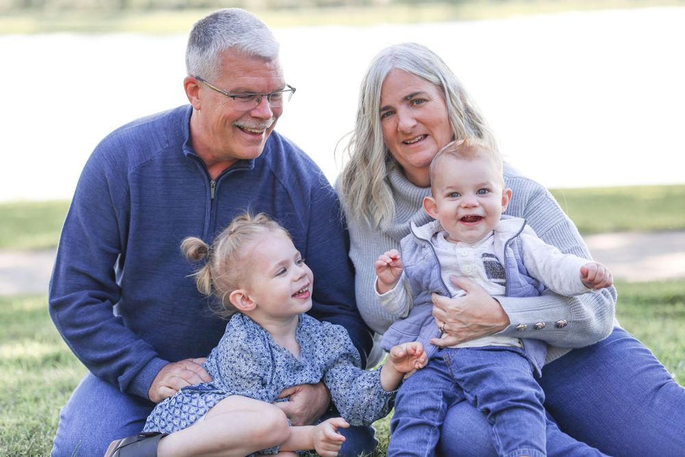 Family sitting and laughing together on grass during outdoor photo session.