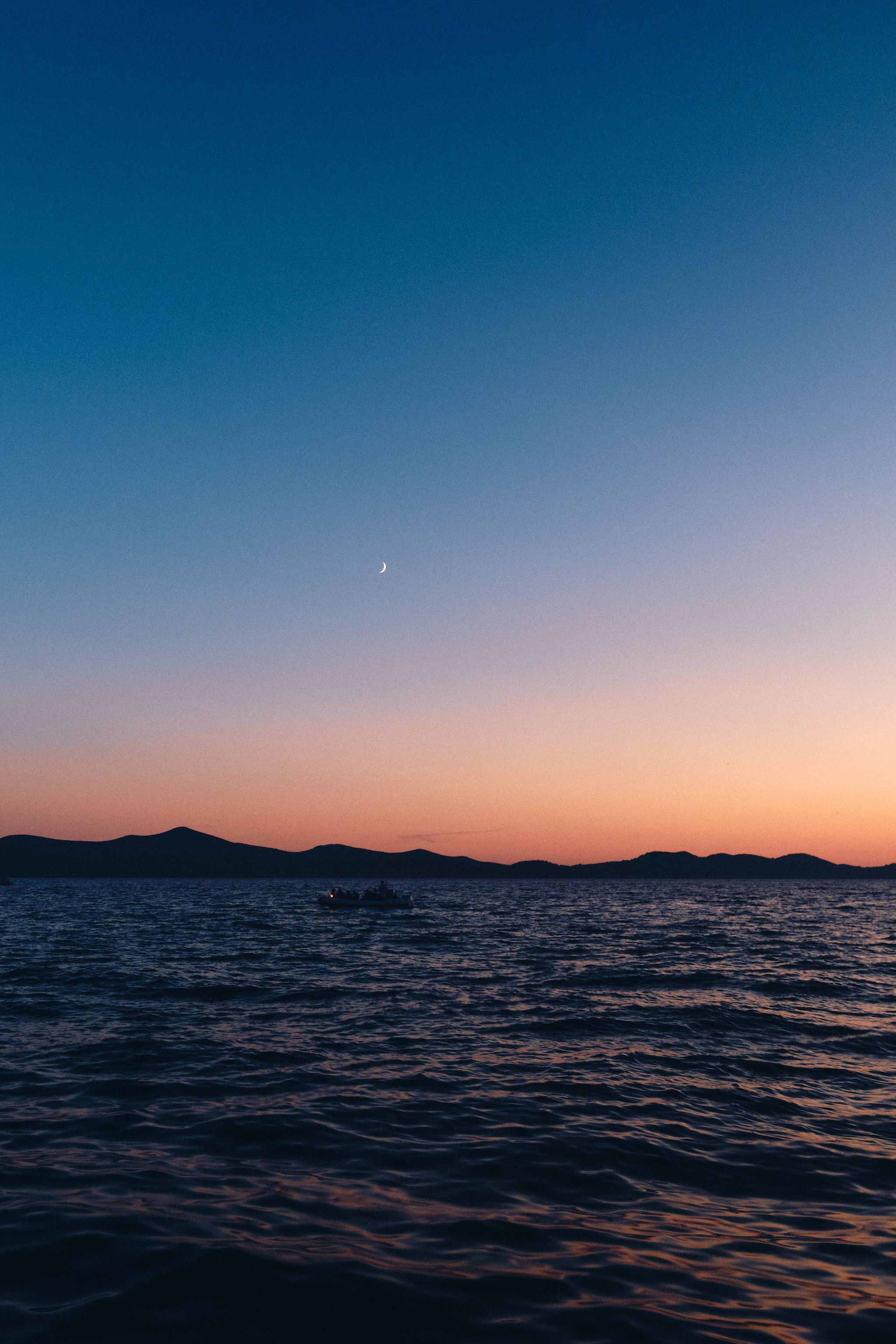 Scenic sunset over mountain silhouettes with calm ocean waters.