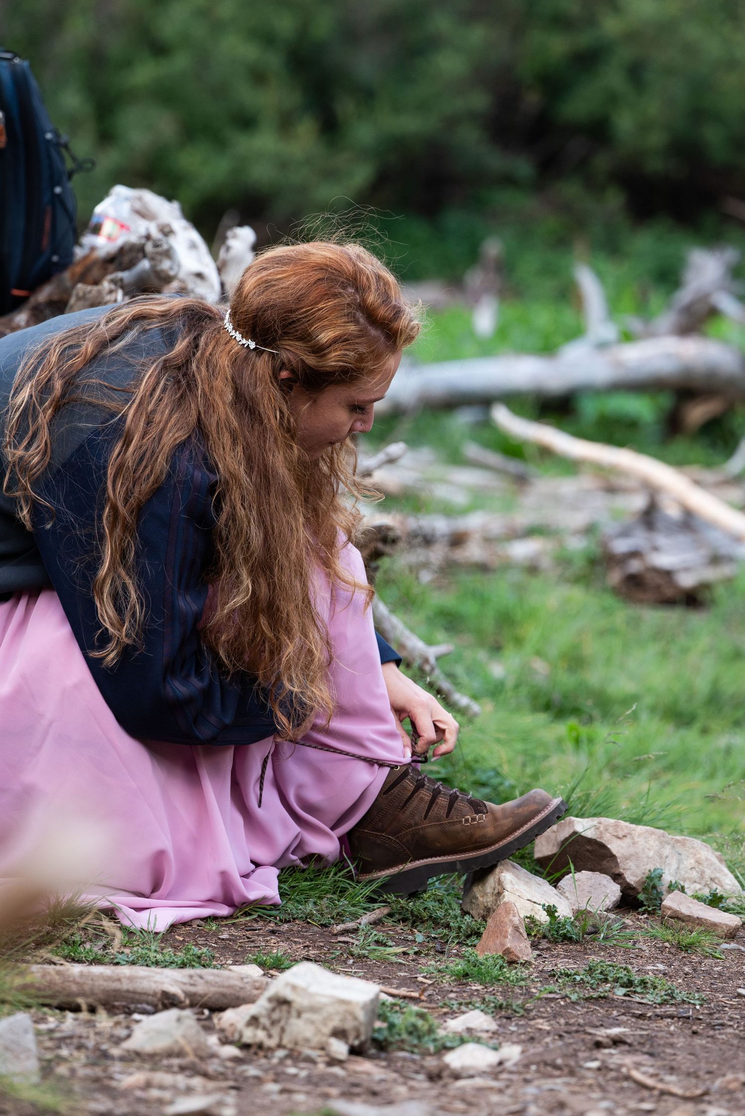 Person in pink dress lying on forest ground surrounded by natural debris.