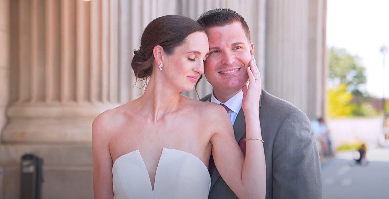 A couple in formal wedding attire embraces intimately on their special day during an outdoor photoshoot.