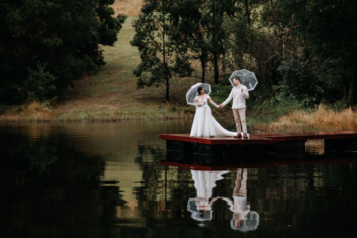Romantic wedding photo on wooden dock with reflection in still lake water.