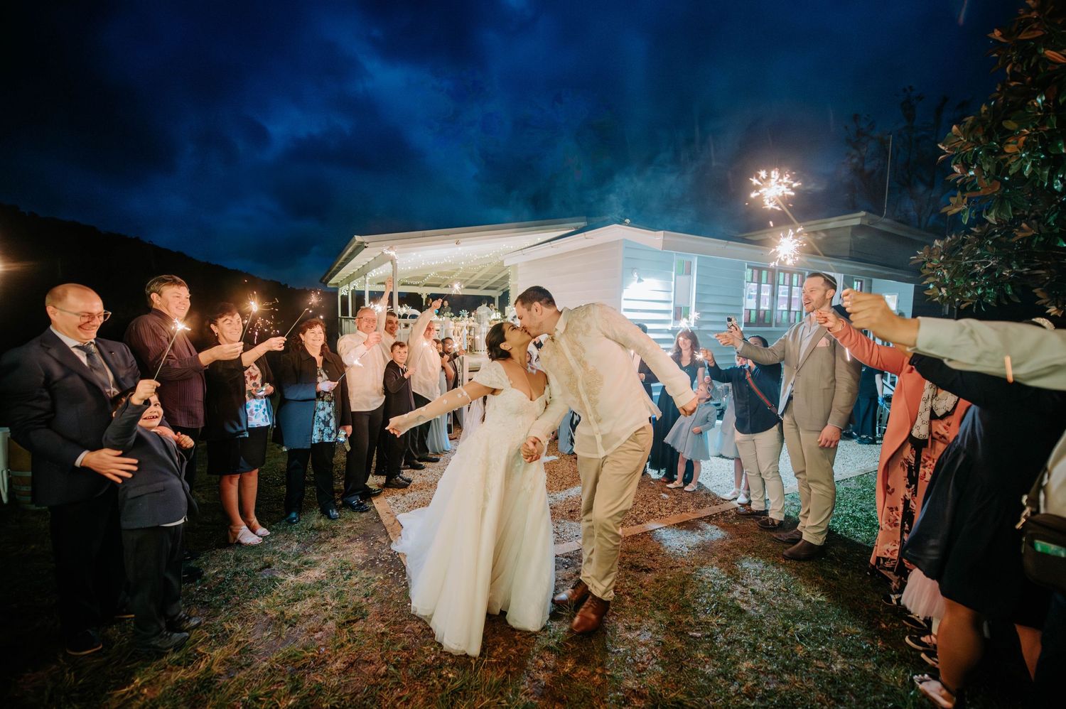 Wedding guests create sparkler exit tunnel for newlyweds during evening celebration.