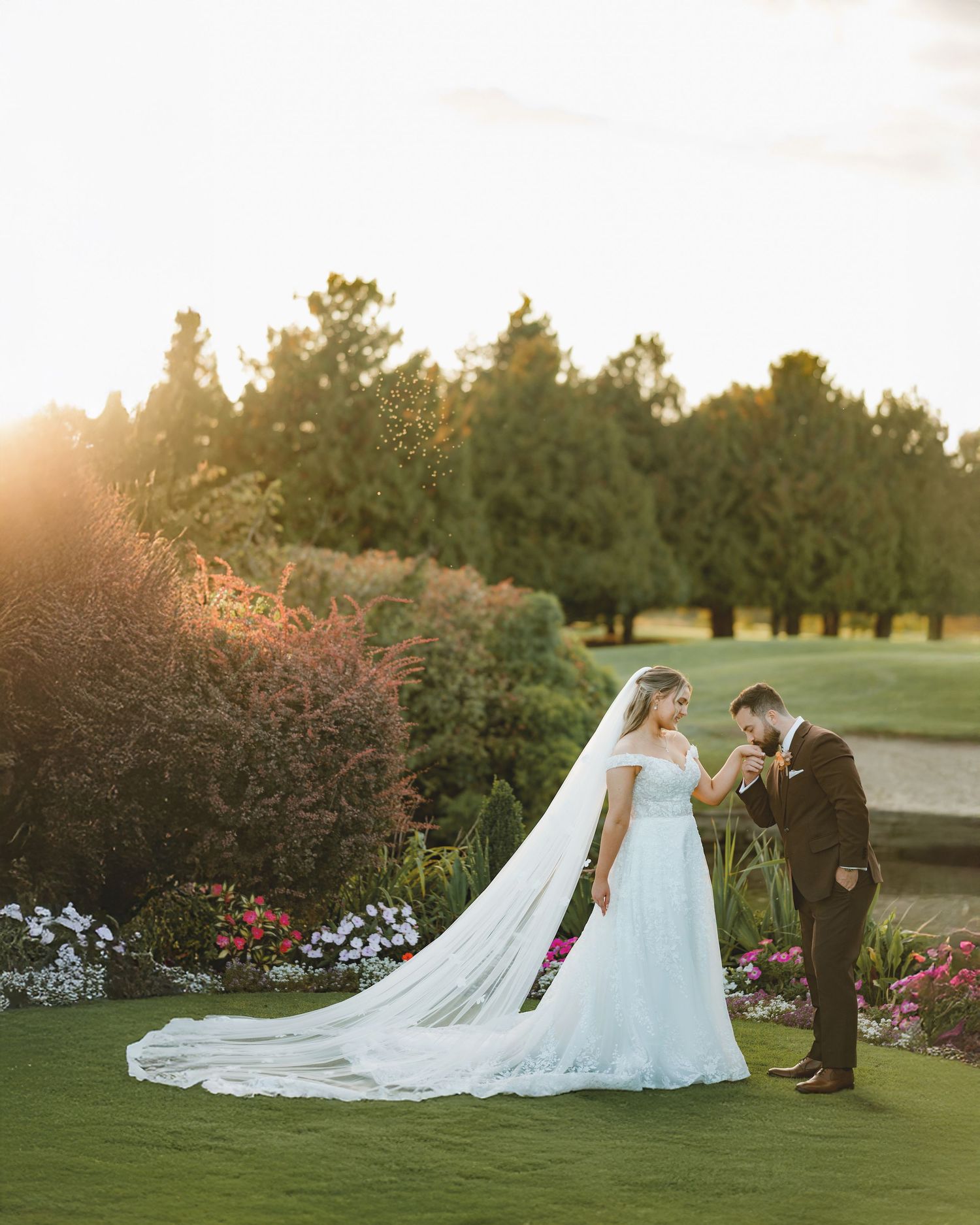 Wedding couple poses in garden setting during golden hour with flowing white dress and veil.