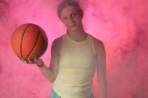 Someone holding a basketball poses against bright pink smoke effects in a studio setting.