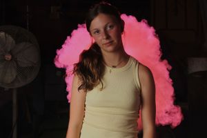Person in a light tank top captured against vibrant pink smoke effects in a studio setting.