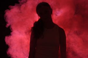 Silhouette poses against intense red smoke effects creating a mysterious atmosphere.