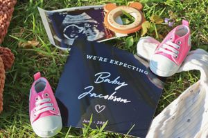 Pink baby shoes and ultrasound photo beside a navy blue pregnancy announcement card reading We're Expecting Baby Jacobson.