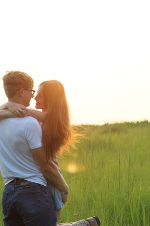 Romantic couple embracing in a green field at golden sunset, sharing an intimate moment outdoors.