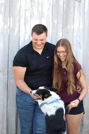Playful moment with a couple and their black and white dog against a rustic wooden fence.