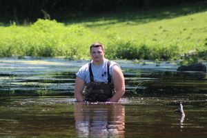Someone wading through shallow water in a sunny outdoor setting with green vegetation.