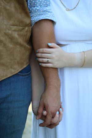 Two hands clasped together showing a close-up of fingers intertwined against a casual dress and denim background.
