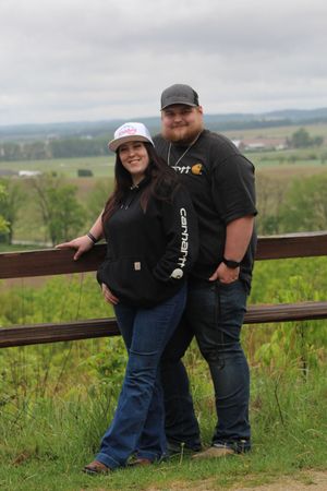 Group poses candidly against rustic wooden railing overlooking scenic rural valley landscape on overcast day.