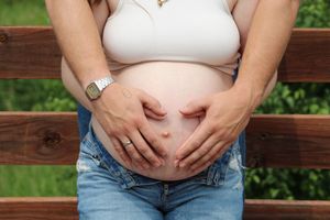 Seven progressive photos showing a growing baby bump during pregnancy against a wooden fence backdrop.
